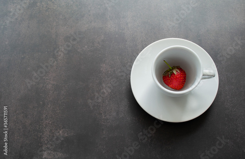 Bright red strawberry berry in a white Cup on a black background. Copy space 