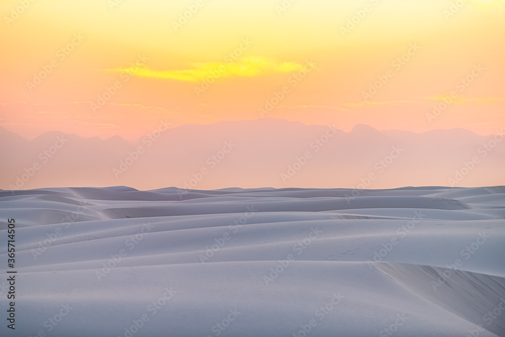 White sands national park monument sand dunes in New Mexico with Organ mountains silhouette on horizon during colorful red yellow sunset