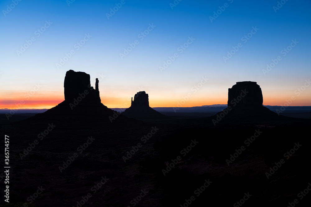 View of Monument Valley buttes silhouette and horizon during blue hour dawn night with sunrise colorful light in Arizona in sky