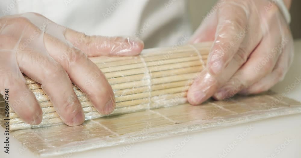 Close up of male chef hands in gloves preparing delicious sushi rolls with avocado in the kitchen Close up of male chef hands in gloves preparing delicious sushi rolls with avocado in the kitchen