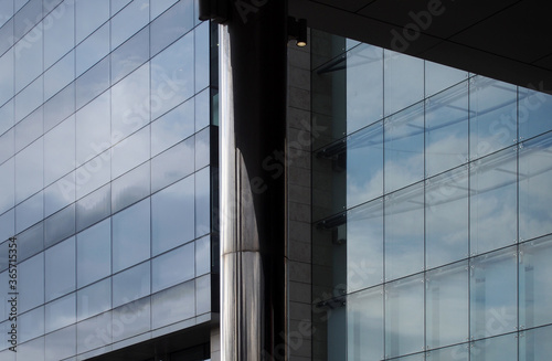modern glass office buildings behind a steel column with blue sky clouds and sunlight reflected in glass windows