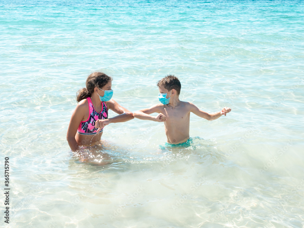 Two children having fun on the beach and wearing protective masks to prevent from coronavirus disease, safe summer holidays concept Two children having fun on the beach and wearing protective masks to prevent from coronavirus disease, safe summer holidays concept
