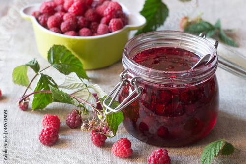 Raspberry jam in glass jar and berries on table