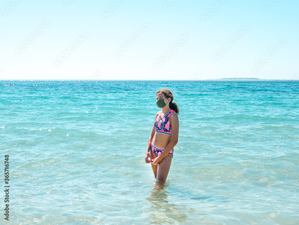 Teenage girl on the beach wearing a protective mask to prevent COVID - 19 or coronavirus disease, safe holidays concept Teenage girl on the beach wearing a protective mask to prevent COVID - 19 or coronavirus disease, safe holidays concept