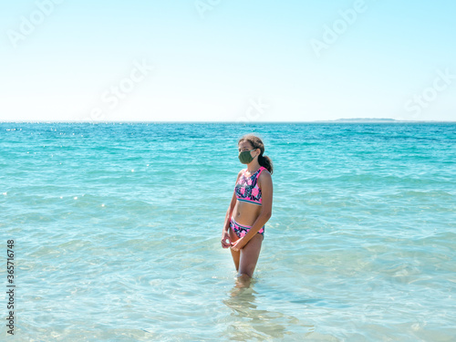 Teenage girl on the beach wearing a protective mask to prevent COVID - 19 or coronavirus disease, safe holidays concept