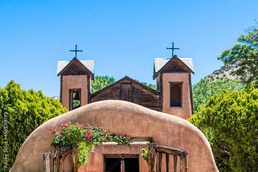 Fototapeta premium Famous historic El Santuario de Chimayo sanctuary church in the United States with entrance gate closeup of flowers in summer