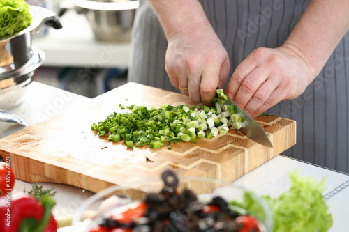 Male Hands Chopping Salad Scallion Ingredient. Chef Cutting Green Onion with Sharp Knife on Wooden Board. Slicing Greens for Dieting Salad with Olive. Culinary Recipe Horizontal Photography
