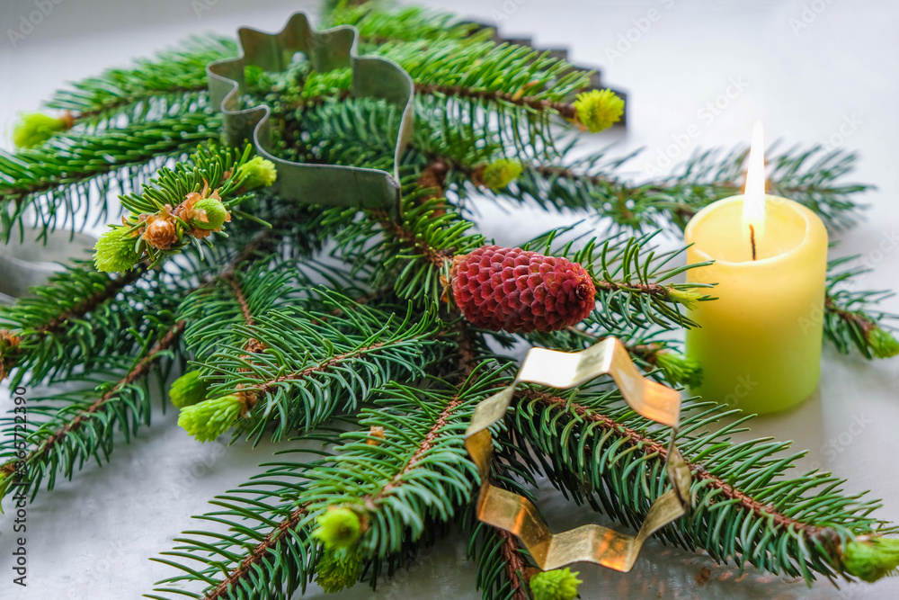 Spruce branch with red cone, Christmas burning candle and metal cookie cutters on a gray background. Home Christmas concept. Spruce branch with red cone, Christmas burning candle and metal cookie cutters on a gray background. Home Christmas concept.