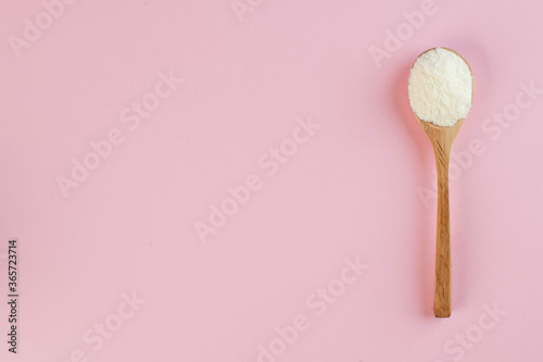  White collagen powder on a wooden spoon on a pink background. Skin care, rejuvenation. Copy space.