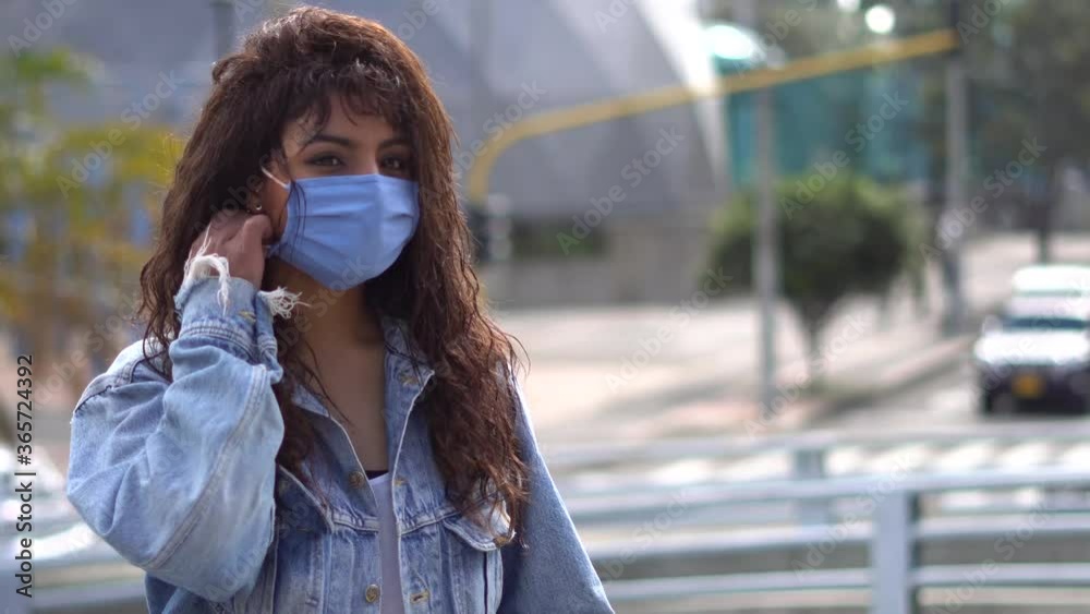 Plano medio de retrato de mujer joven de piel morena mirando fijamente a la cámara se quita el tapa bocas, en tiempos de cuarentena. Aislamiento preventivo, Covid-19.