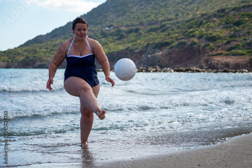 Body positive. Happy plump woman playing ball on the beach. Sports for all