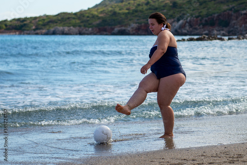 Body positive. Happy plump woman playing ball on the beach. Sport for all