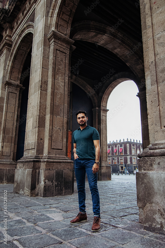Full body portrait of a young latin man standing right in front of a historic mexican building near downtown