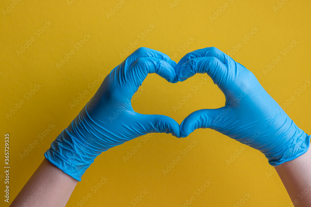 Hands in blue gloves in heart shape on a yellow background. Hands in blue gloves in heart shape on a yellow background.