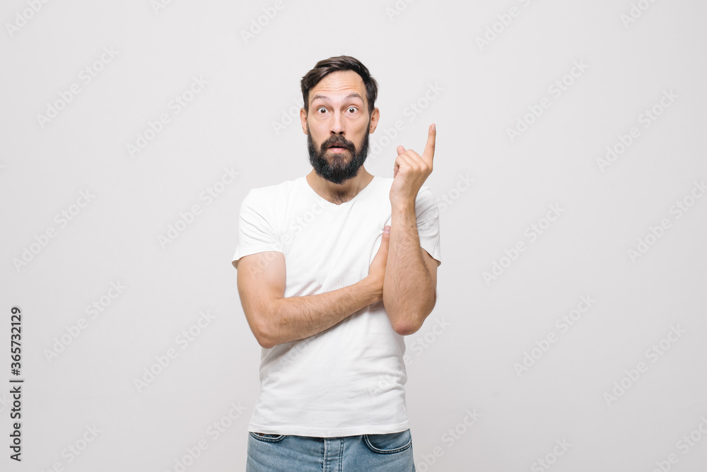 Studio portrait of surprised pretty young man with short haircut standing over white background, looking puzzled to camera with crossed arms on his chest Studio portrait of surprised pretty young man with short haircut standing over white background, looking puzzled to camera with crossed arms on his chest