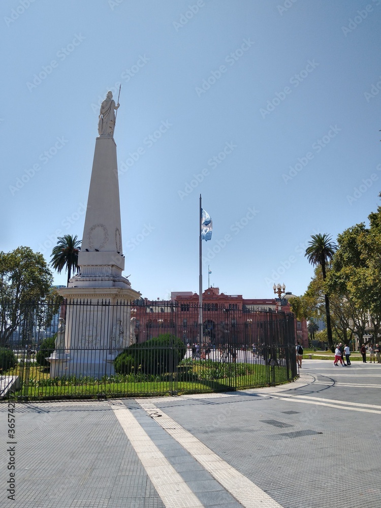 Monument in the middle of a square with a historical building in the background.