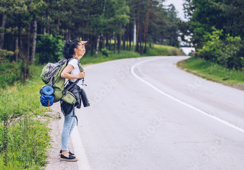 a girl with a backpack stops on the road next to a forest
