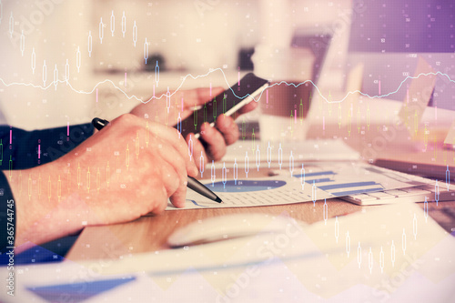 Double exposure of man's hands holding and using a phone and financial graph drawing. Analysis concept.