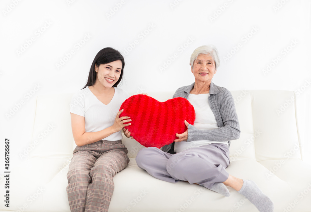 Obraz premium old asian female and young female rest on sofa, old woman hug red heart pillow, they feeling happy and smile, mother's day and family time