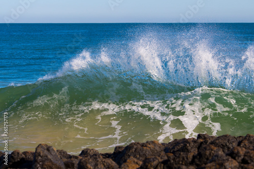 Spectacular, foaming white backwash from the Indian Ocean waves breaking on basalt rocks at Ocean Beach Bunbury Western Australia on a sunny afternoon in winter sends salty spray high into the air.