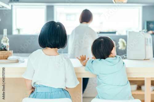 家の中で子供二人が並んで母親の背中を見ている 朝食 食卓 シングルマザー