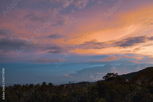 Colorful sunset over forest, village, sea and mountains on a tropical island. View from the top.