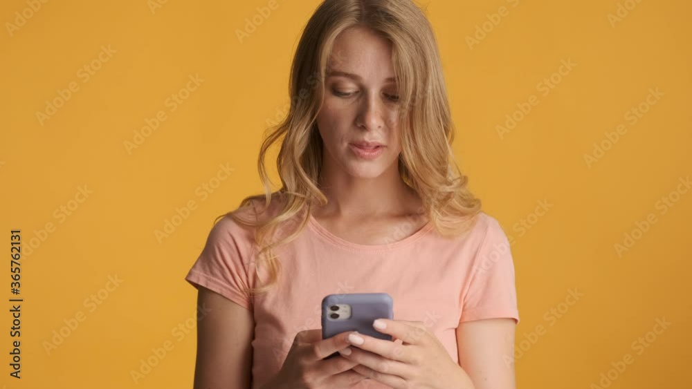 Beautiful blond girl intently using smartphone on camera over colorful background Beautiful blond girl intently using smartphone on camera over colorful background