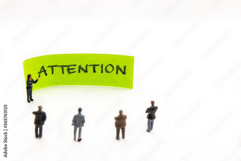 Strategy meeting with miniature figurines posed as business people standing around post-it note with Attention handwritten message on white background, minimalist abstract concept with focus on text Strategy meeting with miniature figurines posed as business people standing around post-it note with Attention handwritten message on white background, minimalist abstract concept with focus on text
