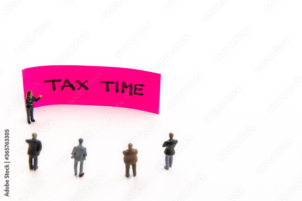 Strategy meeting with miniature figurines posed as business people standing around post-it note with Tax Time handwritten message on white background, minimalist abstract concept with focus on text Strategy meeting with miniature figurines posed as business people standing around post-it note with Tax Time handwritten message on white background, minimalist abstract concept with focus on text