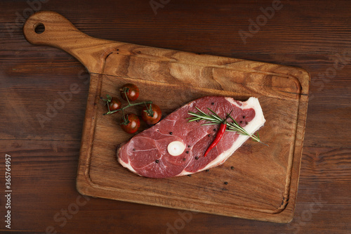 Fresh raw lamb steak on a wooden board with grill spices.