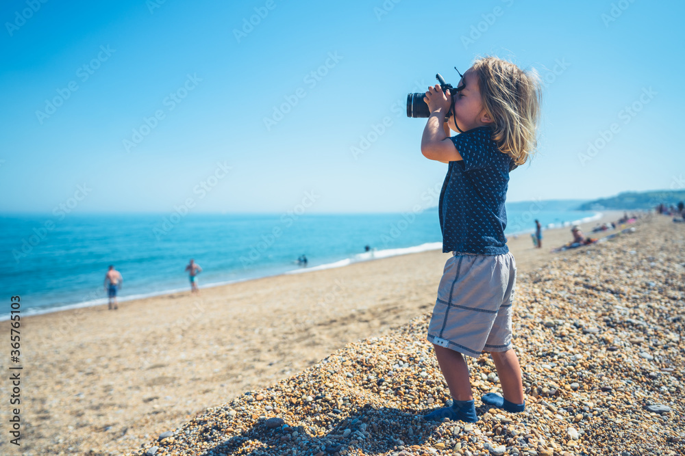 Little preschooler boy taking photos on the beach