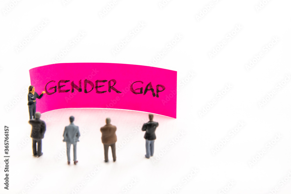 Meeting with miniature figurines posed as business people standing around post-it note with Gender Gap handwritten message in background, minimalist abstract concept with focus on text Meeting with miniature figurines posed as business people standing around post-it note with Gender Gap handwritten message in background, minimalist abstract concept with focus on text