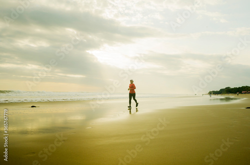 Silhouette of middle aged woman running on the beach - 40s or 50s attractive mature lady doing jogging workout enjoying fitness and healthy lifestyle at beautiful sea sunset