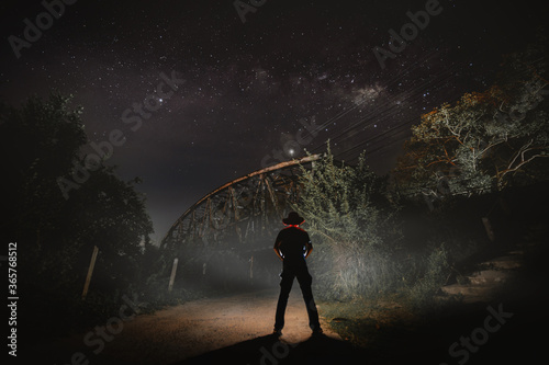 man and railway bridge at night with star background