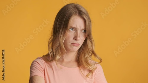Young offended blond woman sadly showing tongue on camera over colorful background