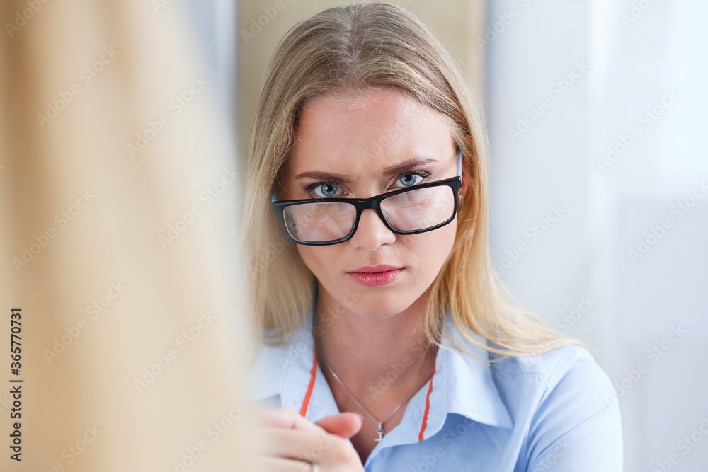 Portrait of serious businesswoman sitting at desk in office and sternly looking at camera Portrait of serious businesswoman sitting at desk in office and sternly looking at camera