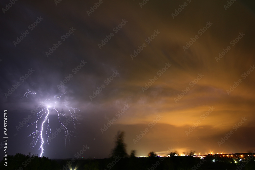 night storm with lightning against the background of light from a chemical plant