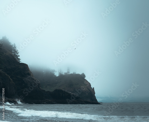 Dark moody lighthouse appears through the mist in the Pacific Northwest.