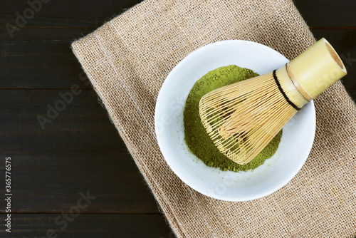 Matcha, green tea powder with bamboo whisk on wooden background