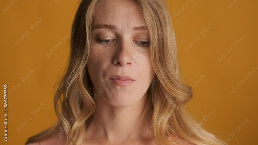 Close up funny blond girl dreamily chewing gum on camera over colorful background. Face expression
