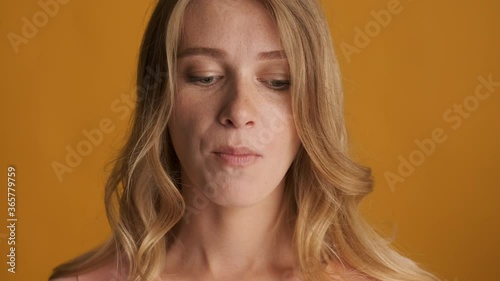 Close up funny blond girl dreamily chewing gum on camera over colorful background. Face expression