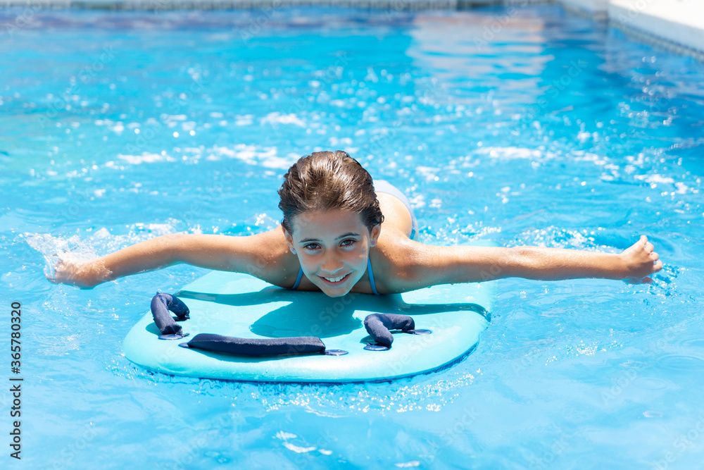 Cute girl playing with a bodyboard in a swimming pool.