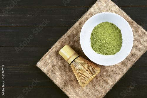 Matcha, green tea powder with bamboo whisk on wooden background