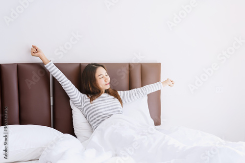 Tableau sur toile Young asian woman sitting on the bed and stretch oneself in the morning