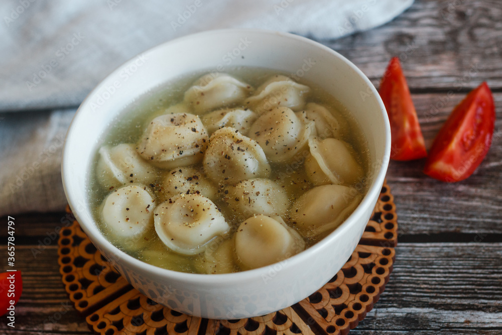 Dumplings with broth in a plate. Traditional Russian dish. Pelmeni with tomatoes on a wooden table Dumplings with broth in a plate. Traditional Russian dish. Pelmeni with tomatoes on a wooden table