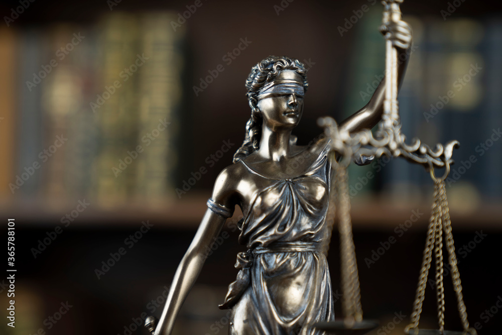 Law theme. Judge chamber. Themis statue on brown shining desk. Collection of legal books in the bookshelf. Law theme. Judge chamber. Themis statue on brown shining desk. Collection of legal books in the bookshelf.
