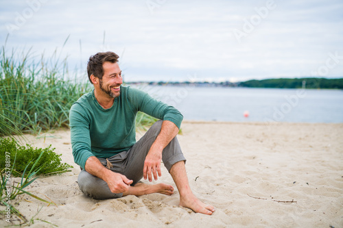 Bestager Mann sitzt am Strand und lächelt in sich hinein mit viel platz drumherum  