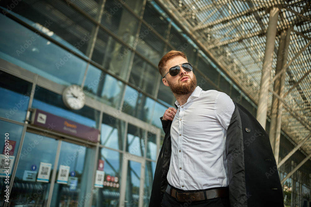 Close up of businessman putting on raincoat in city, man puts coat outside, boss or worker black suit. Serious pensive person standing sunglasses. Handsome young male office jacket. Glasses wearing Close up of businessman putting on raincoat in city, man puts coat outside, boss or worker black suit. Serious pensive person standing sunglasses. Handsome young male office jacket. Glasses wearing