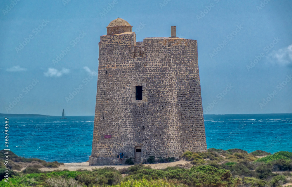 A man is sitting in front of defence tower at Ses Salines beach at Ibiza, Spain.