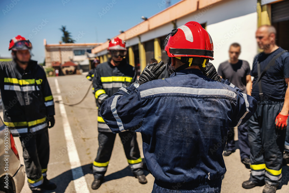 Group of firemen standing outdoors in protective uniforms and helmets and preparing for action. Group of firemen standing outdoors in protective uniforms and helmets and preparing for action.